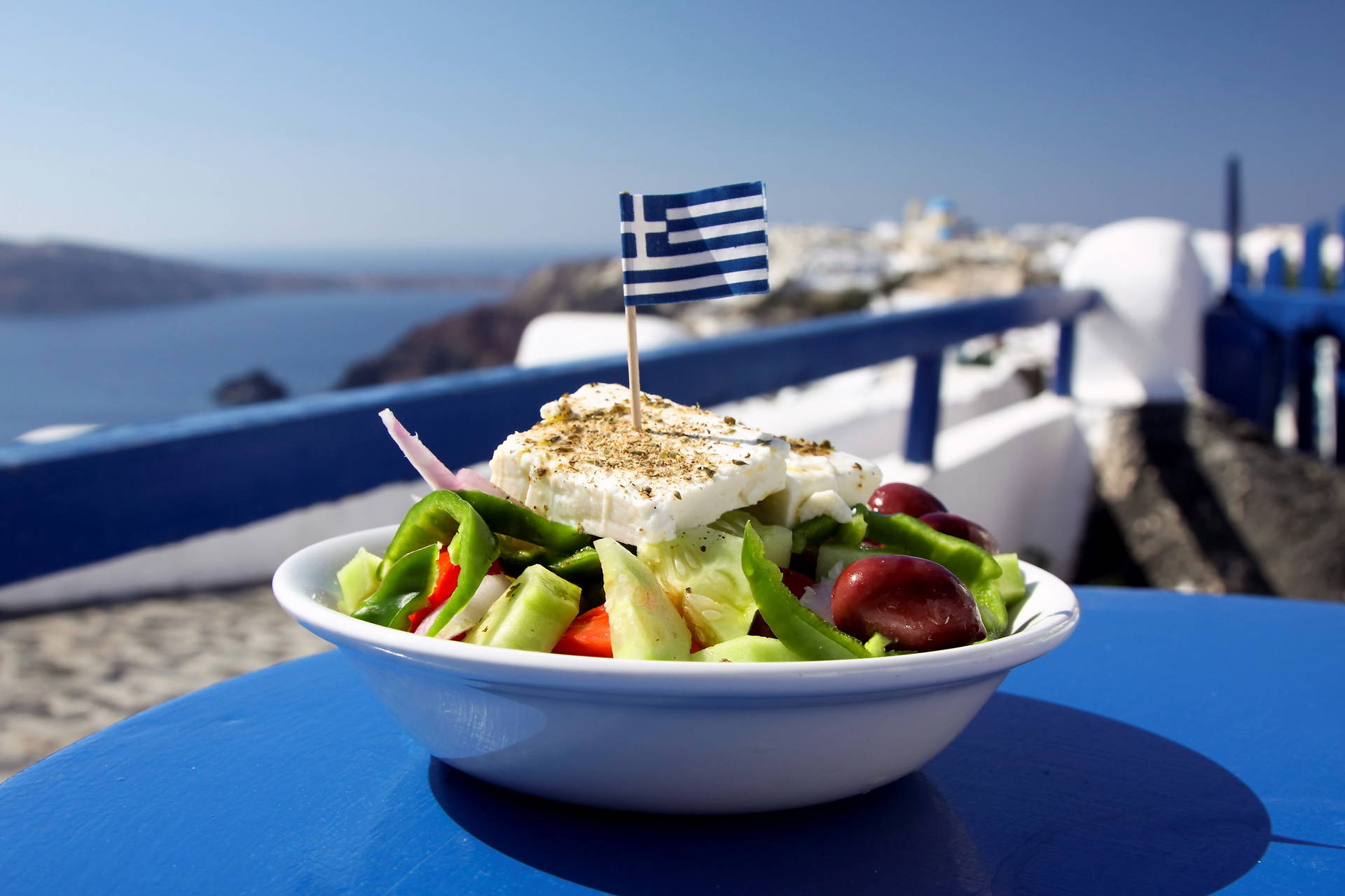 Sałatka grecka na tle Santorini i greckiej flagi.