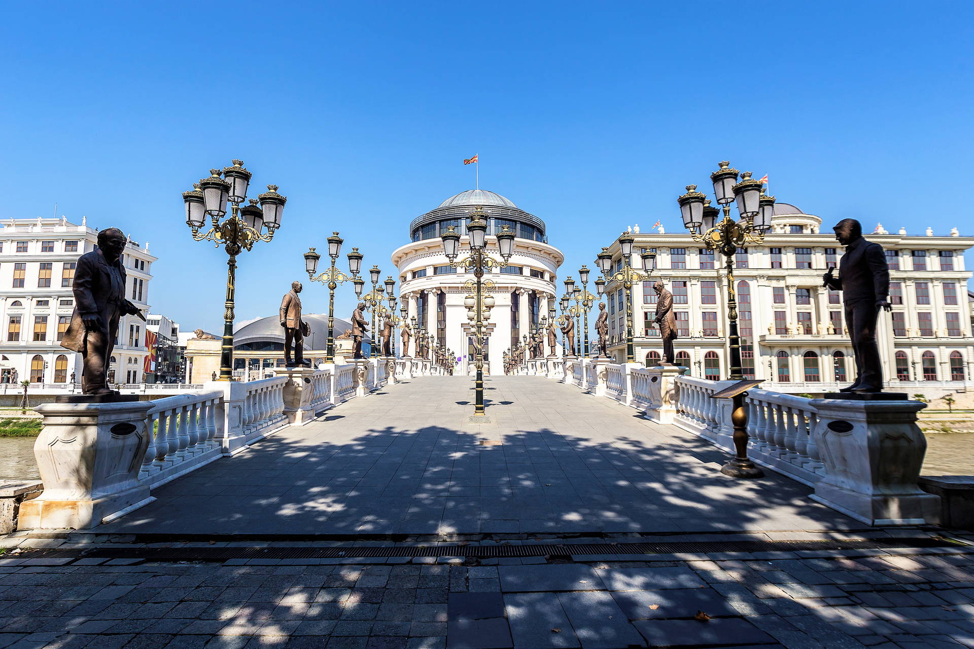 Kamienny Most Sztuki w Skopje, Macedonia Północna. Most zdobią rzeźby i latarnie. W tle widoczny budynek z kopułą.