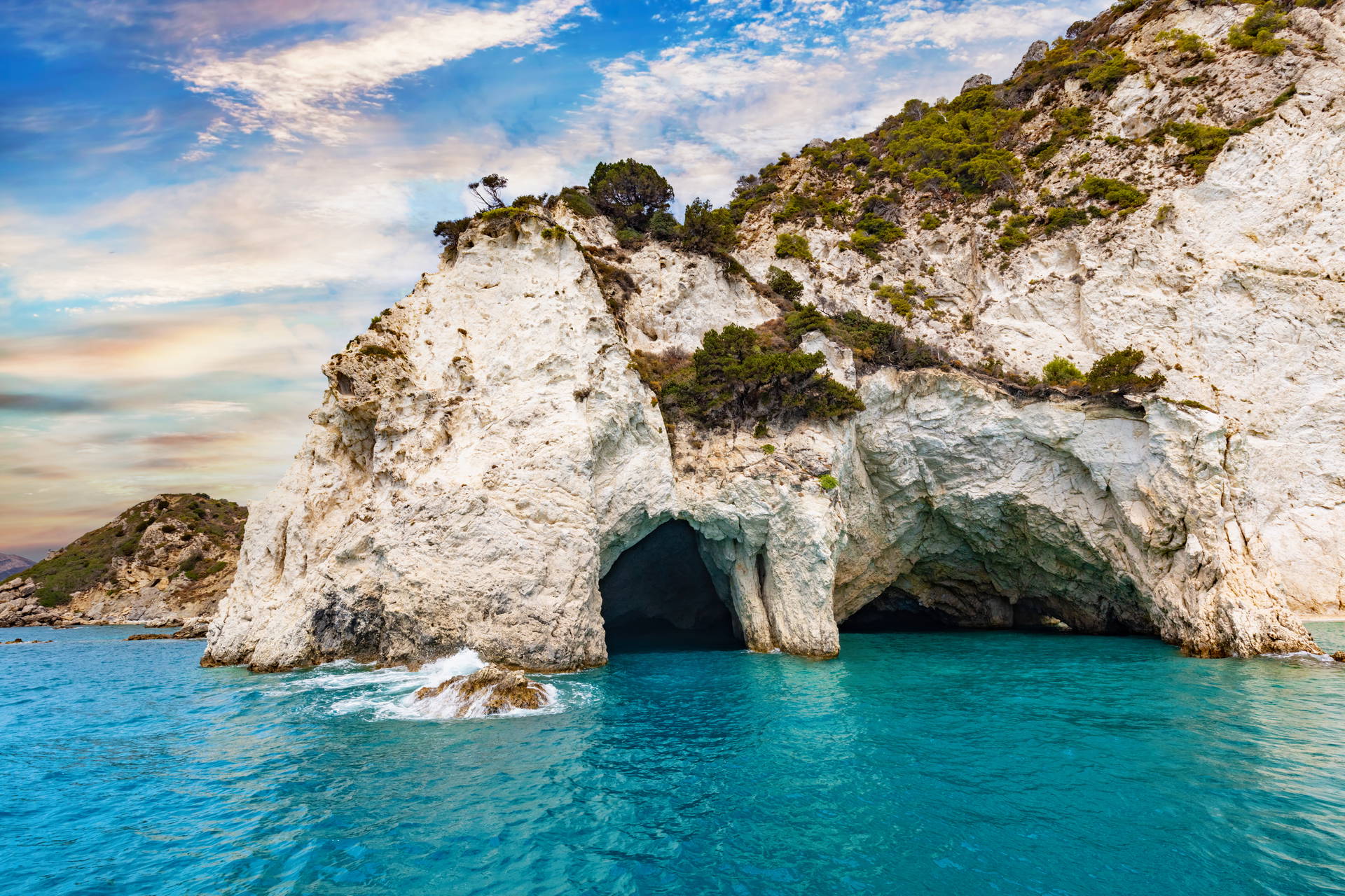 Turkusowa woda obmywa klify z jaskiniami na wyspie Zakynthos.