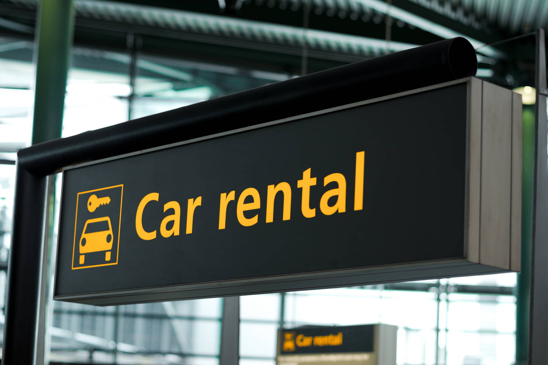 Czarny znak na lotnisku z żółtym napisem „Car rental” i symbolem samochodu z kluczem.