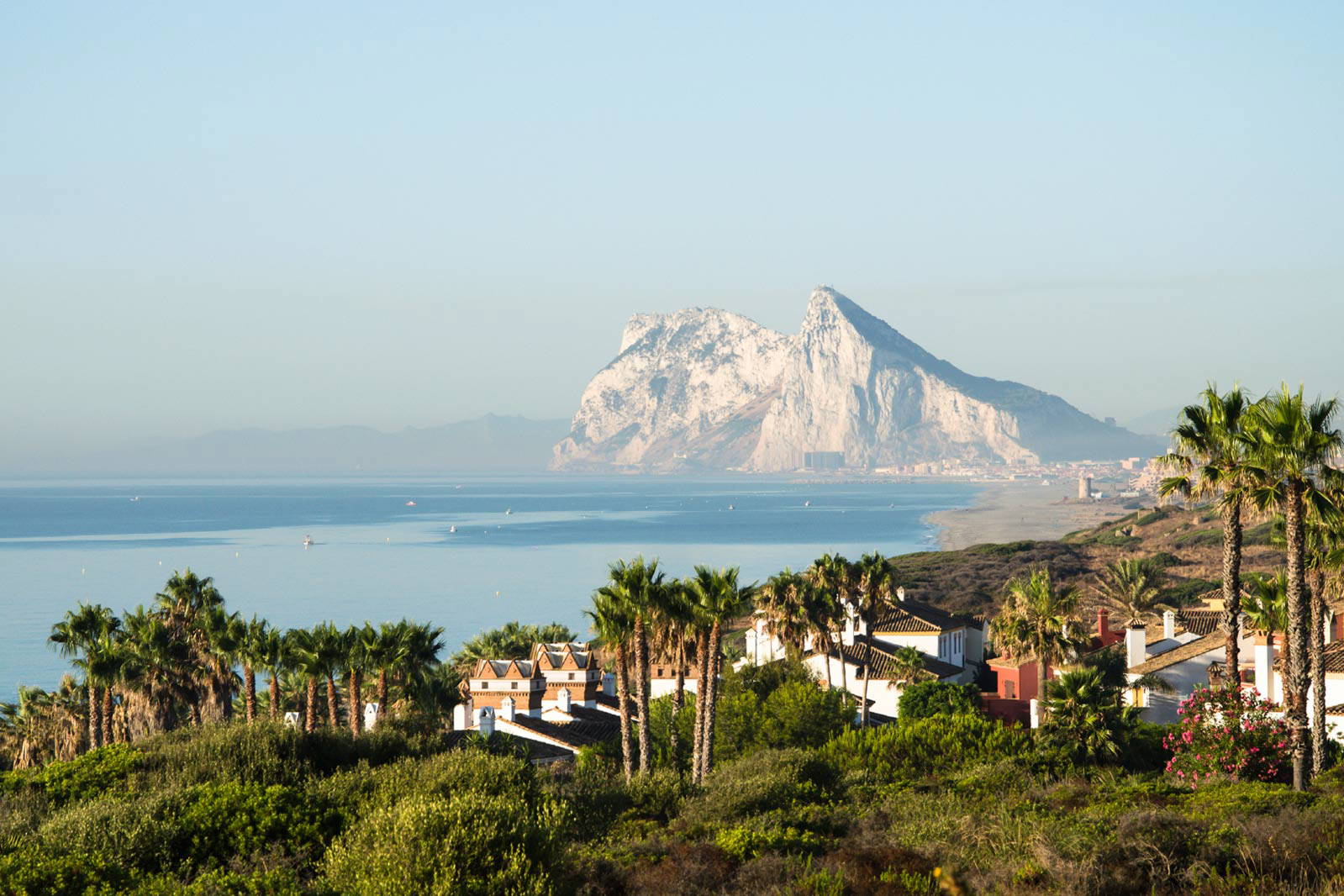 Skała Gibraltar z wybrzeżem, domami i palmami na pierwszym planie.