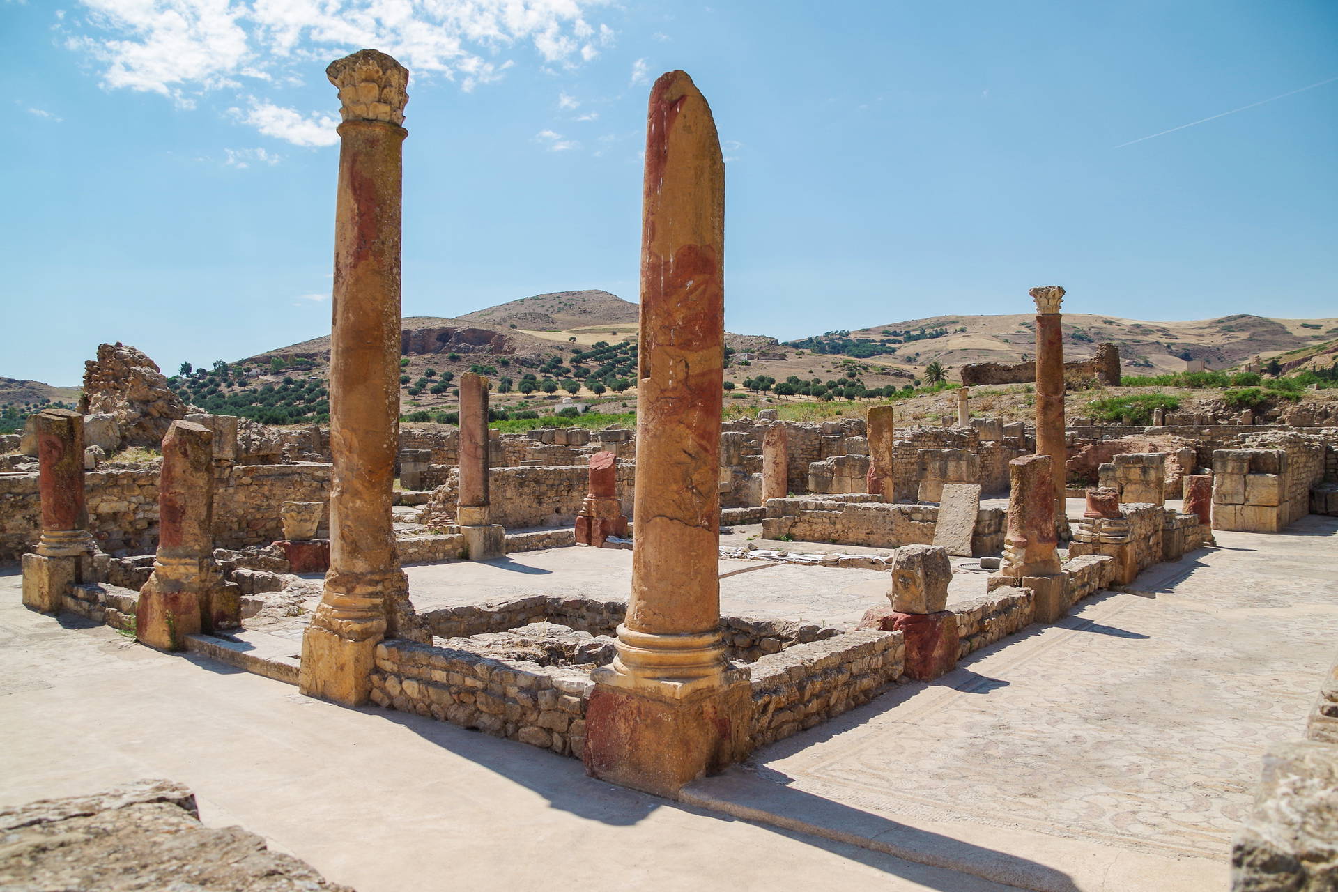 Ruiny starożytnego miasta Dougga w Tunezji. Widoczne kolumny i fragmenty murów na wzgórzu.
