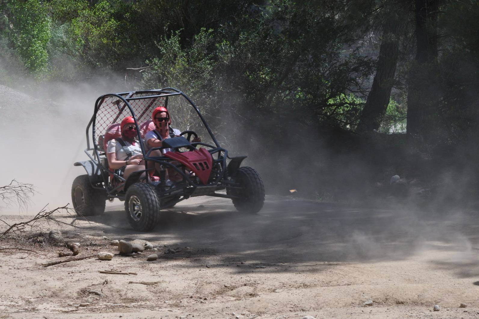 Dwie osoby jadą buggy po piaszczystej drodze.