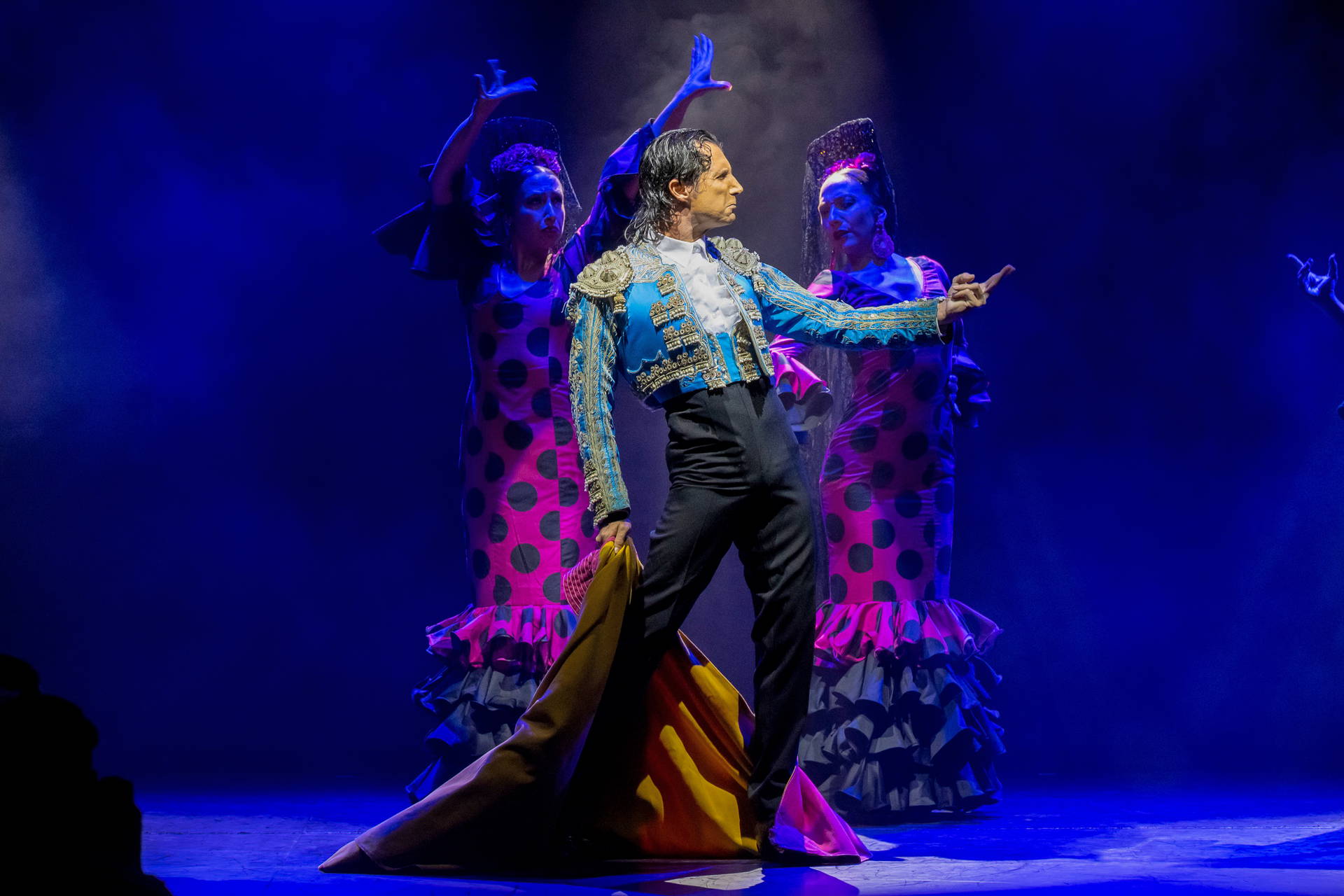 Tancerz flamenco w tradycyjnym stroju i dwie tancerki za nim.