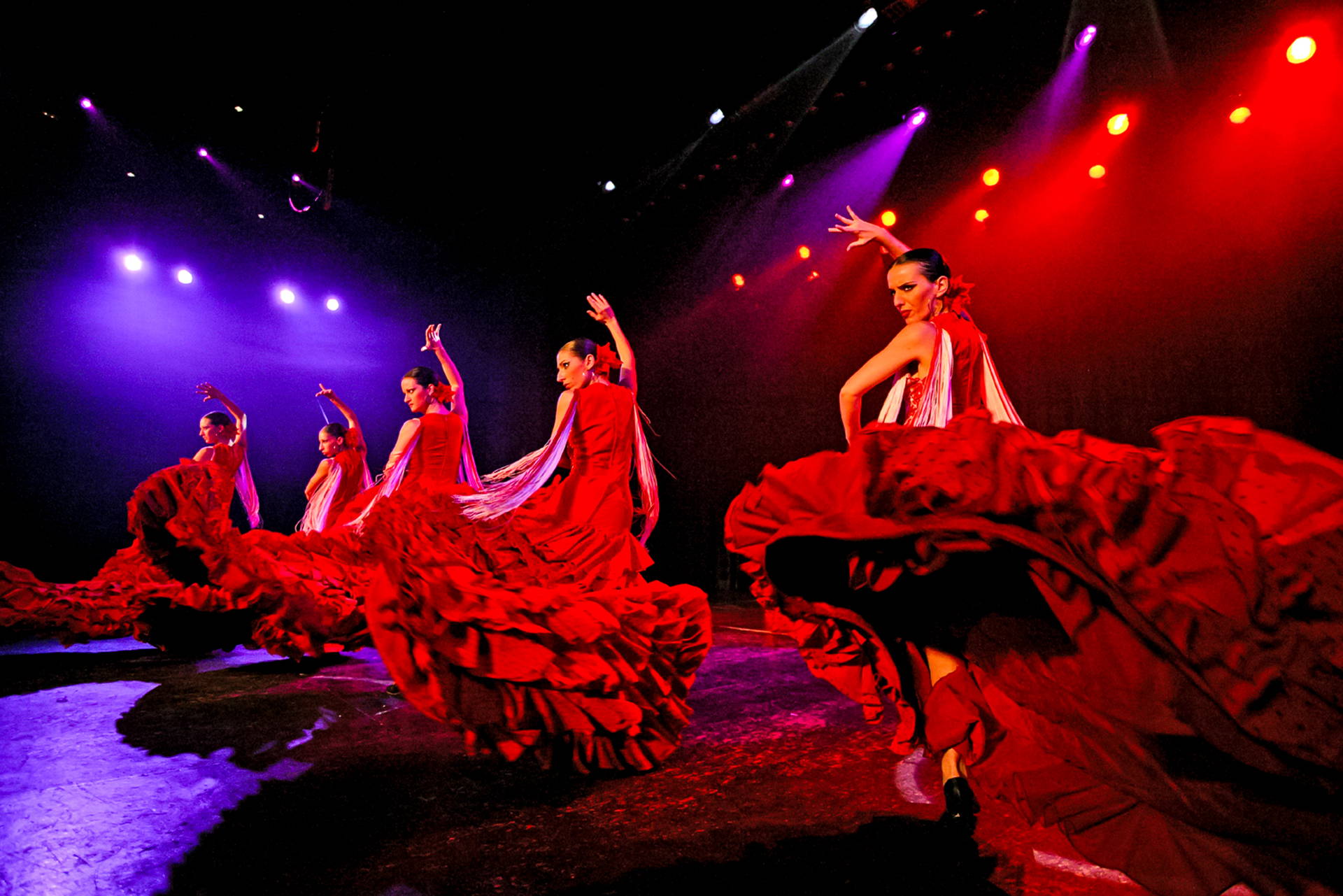 Tancerki flamenco w czerwonych sukniach występują na scenie.