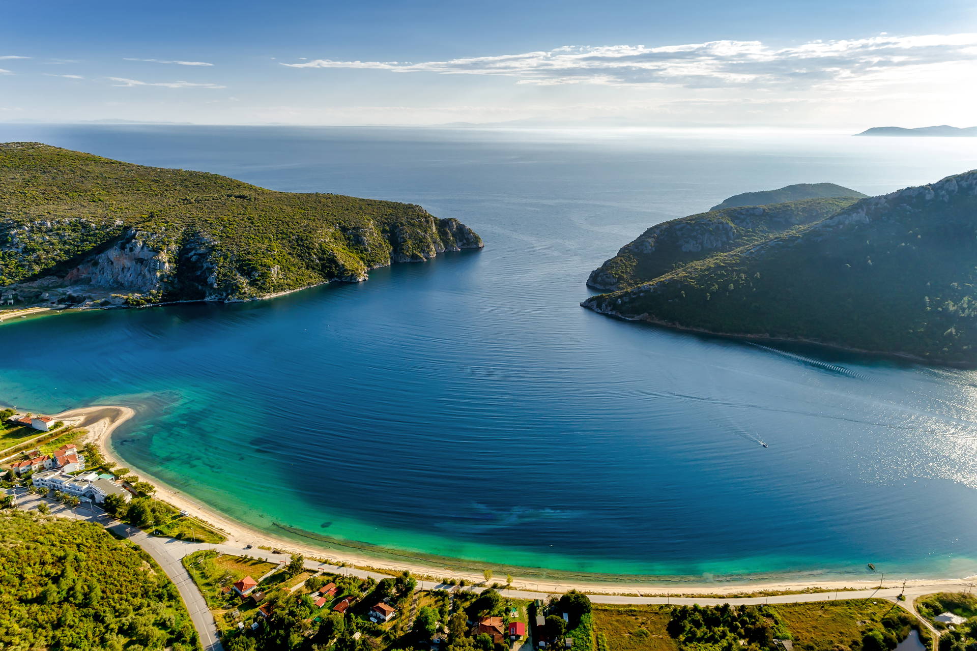 Widok z lotu ptaka na zatokę z plażą i zielonymi wzgórzami w tle.
