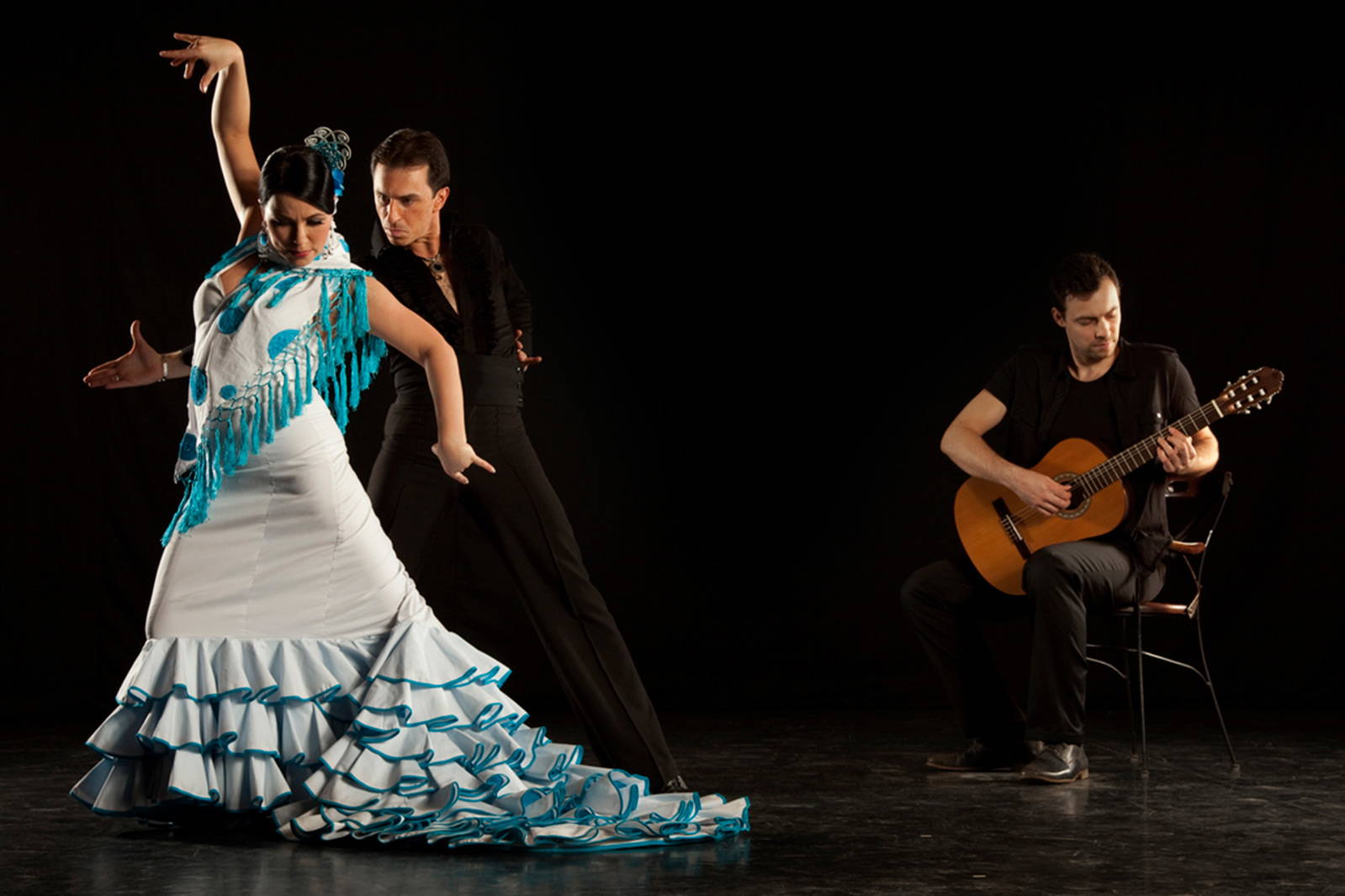 Tancerka i tancerz flamenco w trakcie występu. W tle gitarzysta.