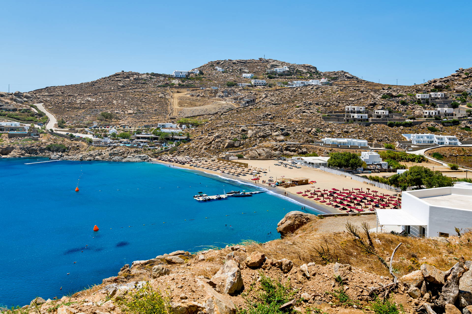 Widok z góry na plażę na Mykonos z czerwonymi parasolami.