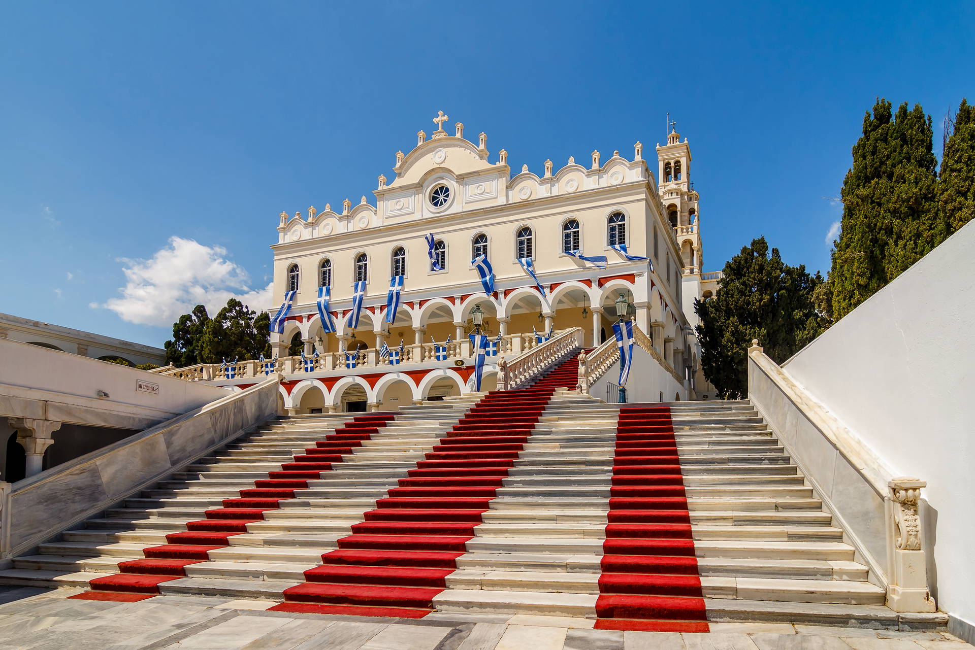 Kościół Panagia Evangelistria na wyspie Tinos ze schodami pokrytymi czerwonym dywanem.