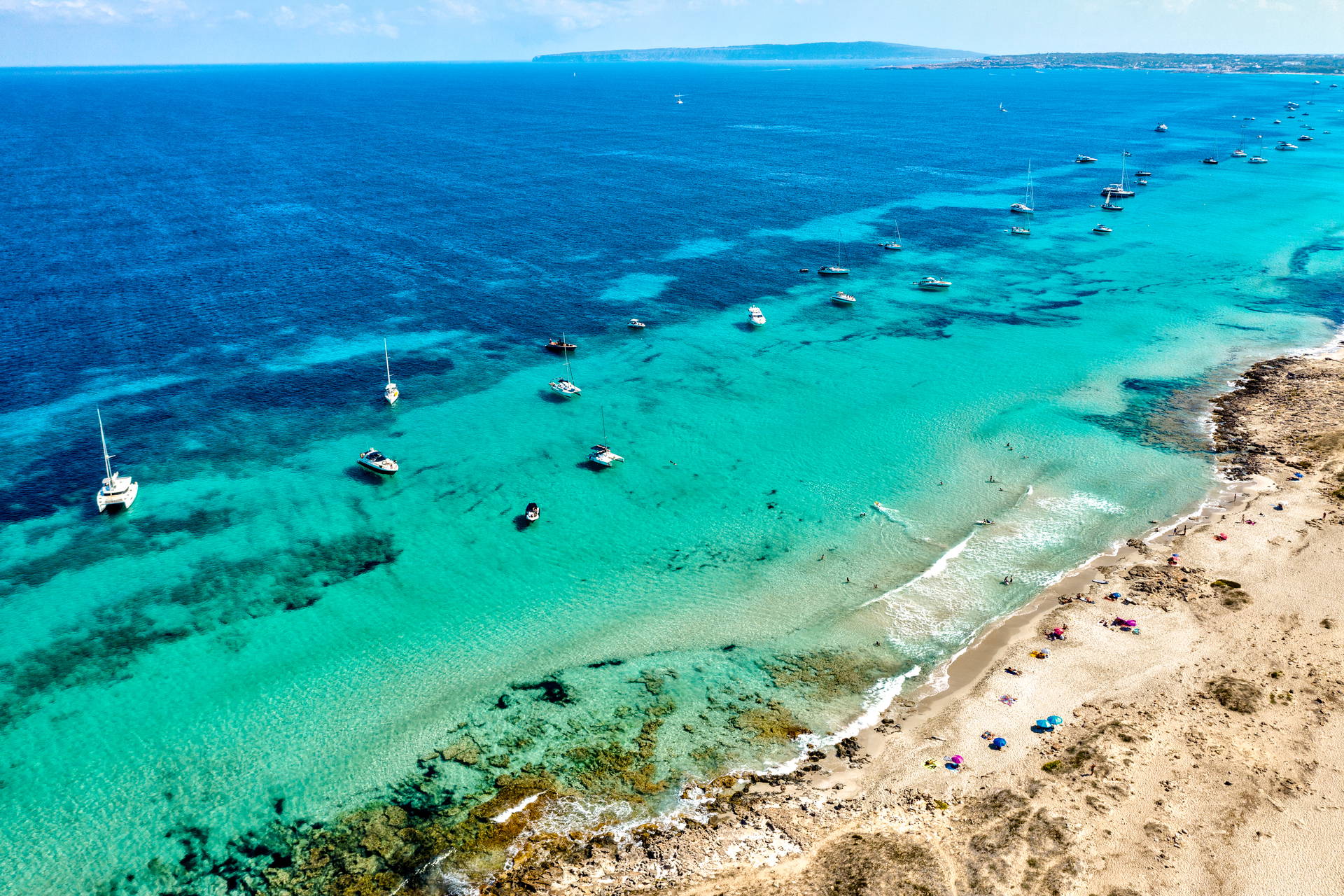 Widok z lotu ptaka na plażę Ses Illetes na Formenterze: turkusowa woda, łodzie i ludzie na piasku.