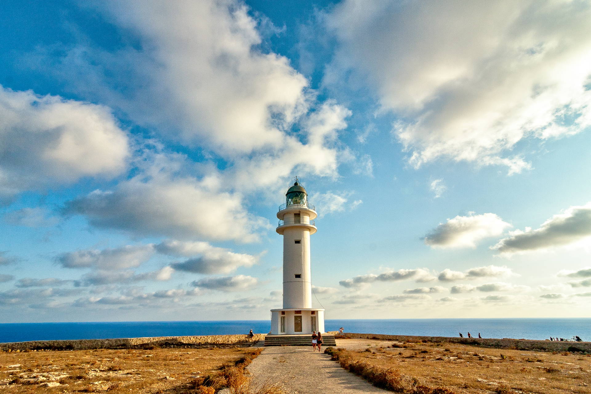Biała latarnia morska na klifie Cap de Barbaria na Formenterze. W tle błękitne morze i niebo z białymi chmurami.