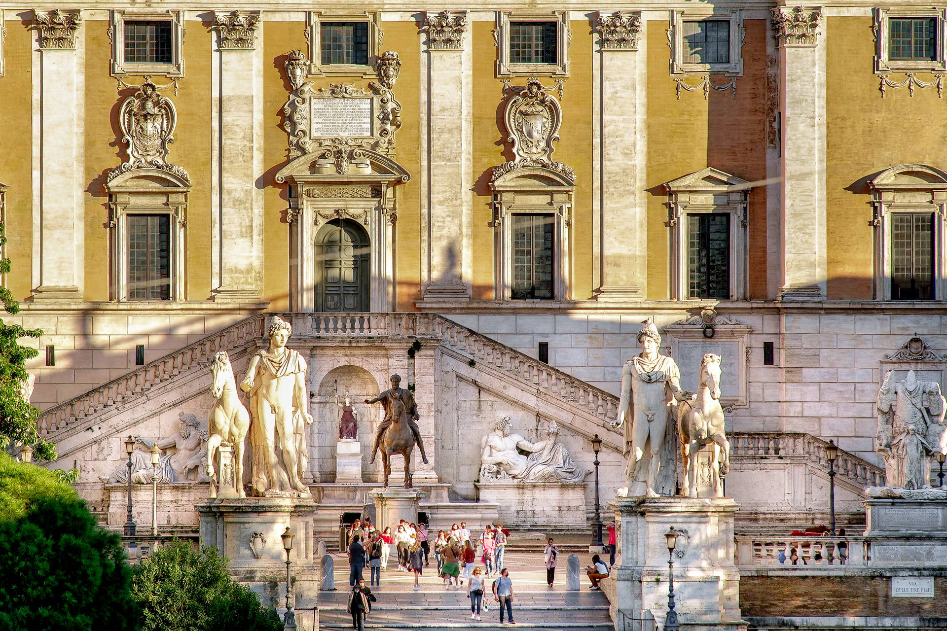 Kapitol w Rzymie z rzeźbami i turystami na schodach.
