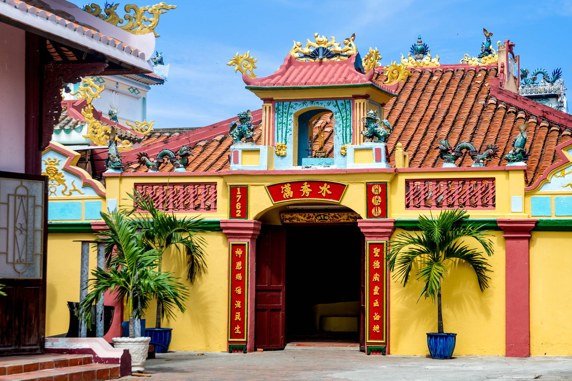 Kolorowy budynek świątyni z czerwonymi drzwiami i palmami w donicach.