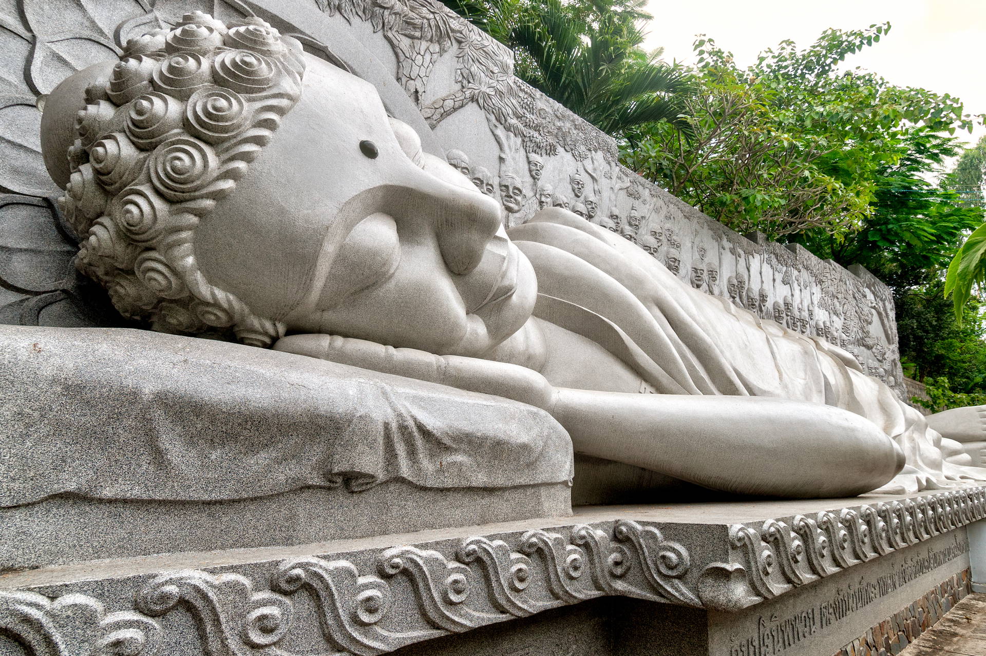 Posąg leżącego Buddy na kamiennym cokole.