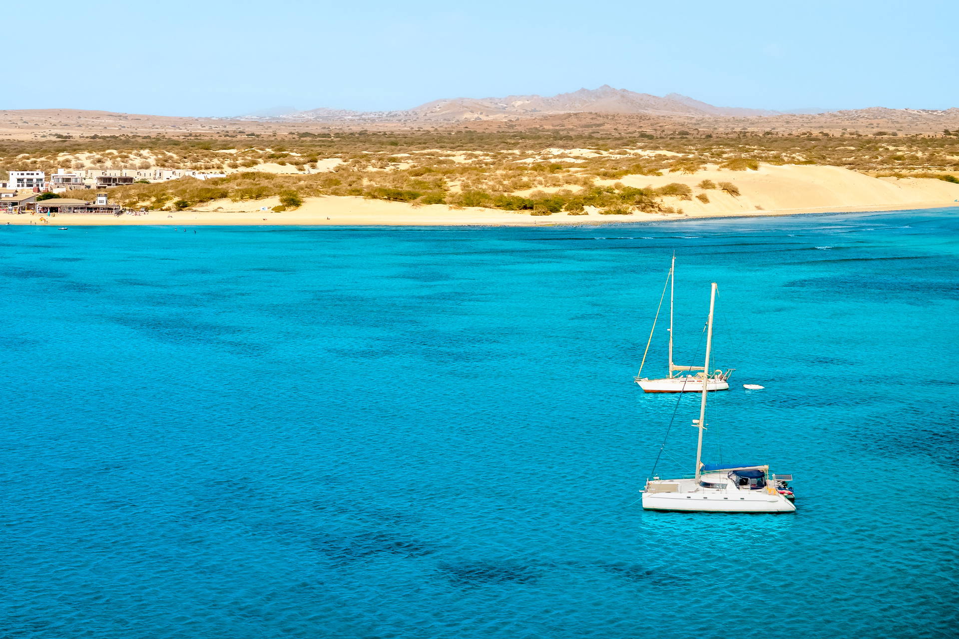Dwa jachty na turkusowym morzu przy piaszczystej plaży na wyspie Boa Vista. W tle widać miasto.