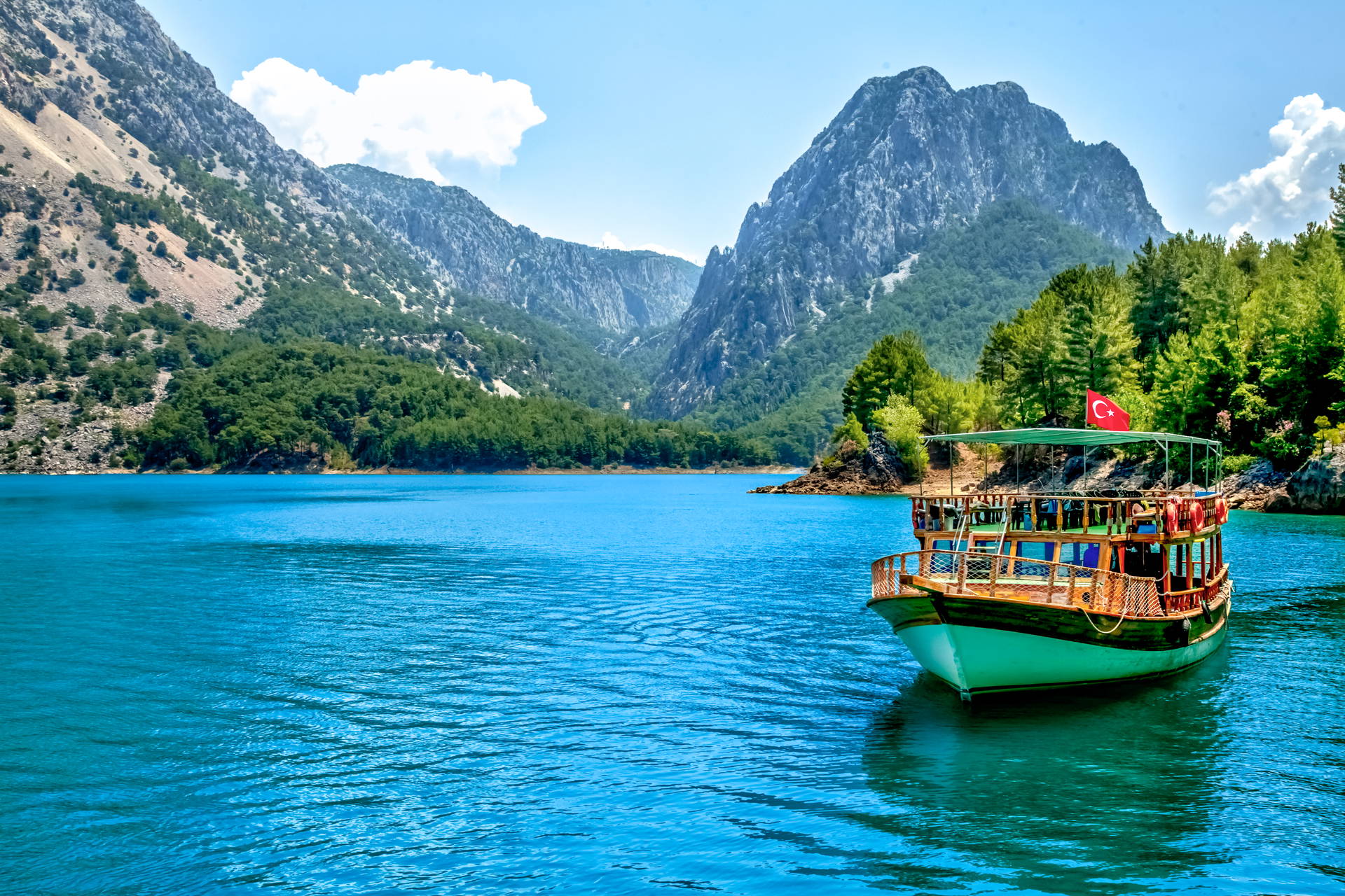 Statek wycieczkowy z turecką flagą w Zielonym Kanionie, pośród zalesionych gór.