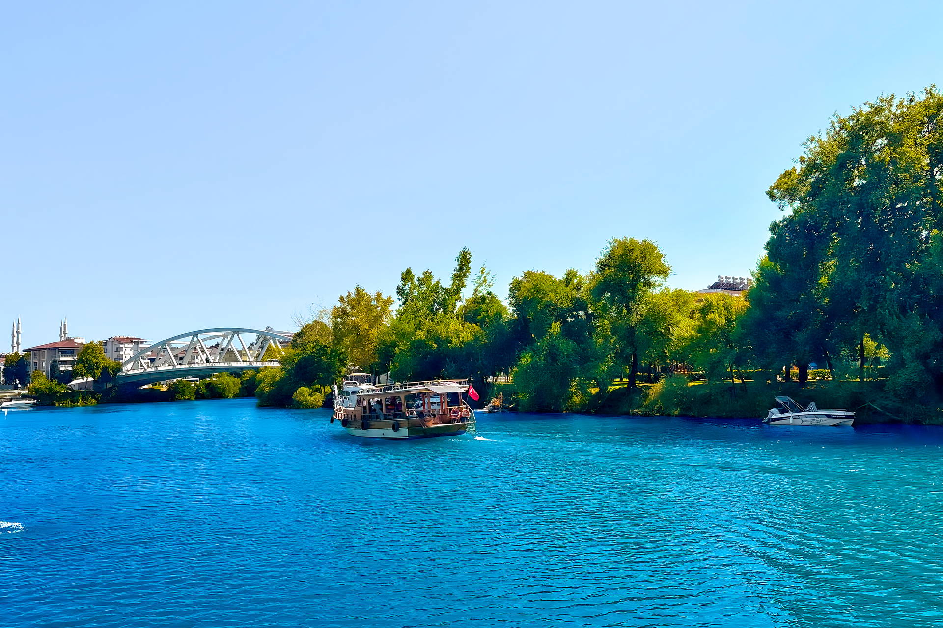Statek wycieczkowy płynie po turkusowej rzece Manavgat w Turcji. W tle widać most i miasto.