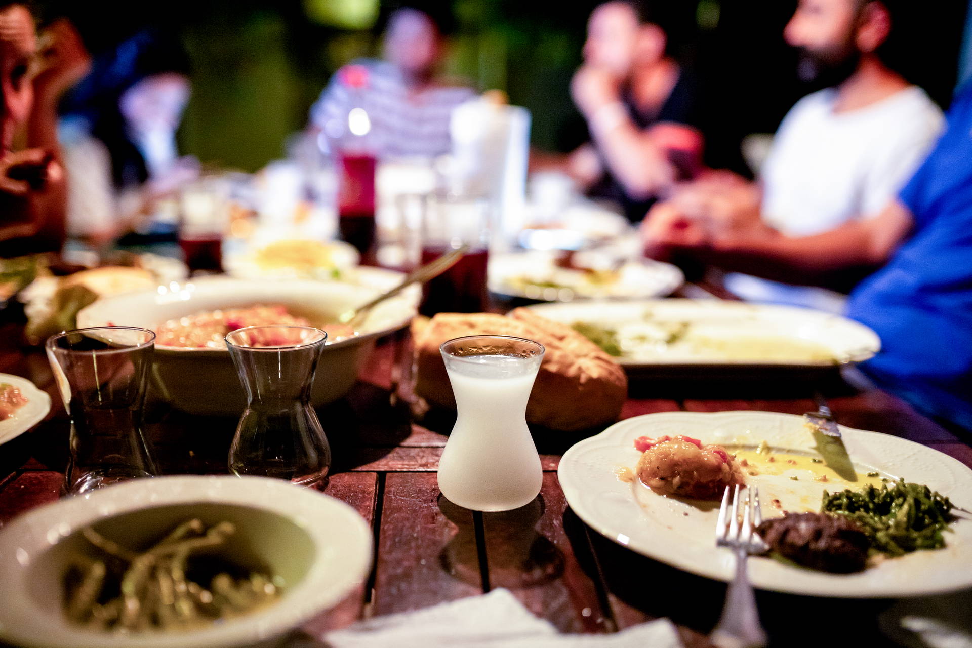 Stół zastawiony tureckimi potrawami i szklaneczką rakı. W tle biesiadują goście.