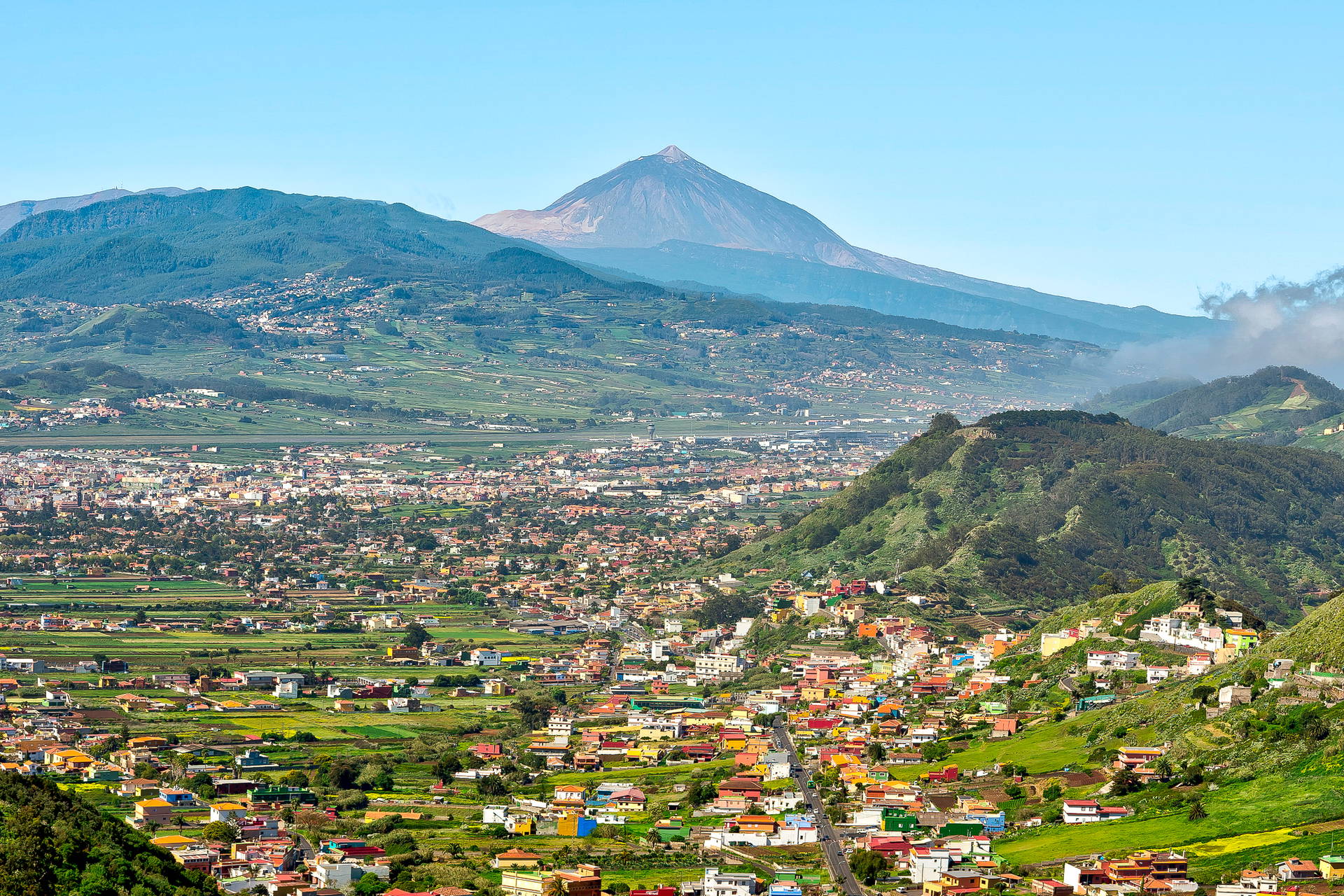 Krajobraz Teneryfy: miasto w dolinie i zielone wzgórza, a w tle wulkan Teide.