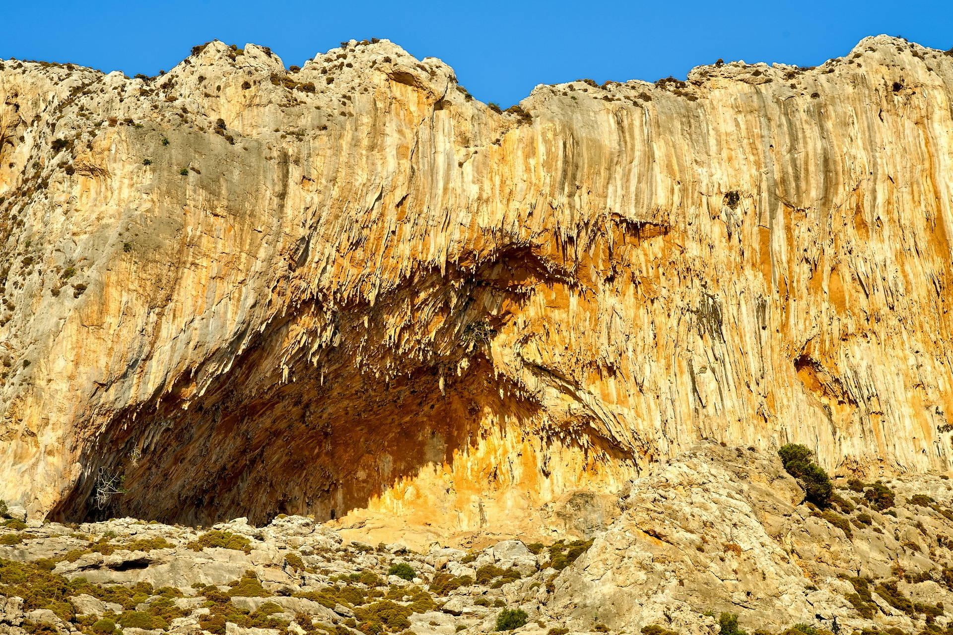 Masywny, pomarańczowy klif z jaskinią Grande Grotta na Kalymnos, na tle błękitnego nieba.