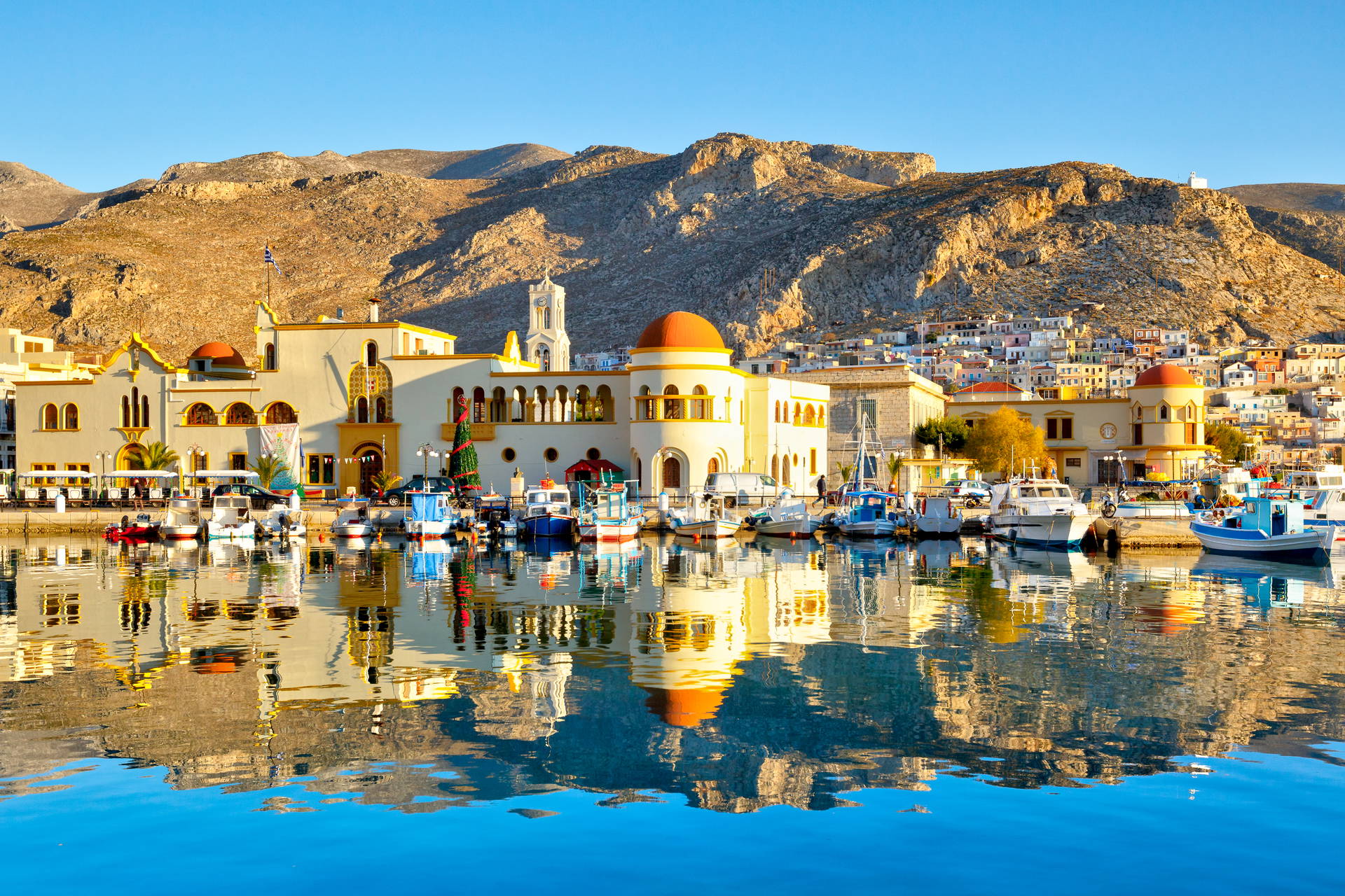 W porcie Pothia na Kalymnos zacumowane łodzie i budynki odbijają się w wodzie na tle skalistych gór.