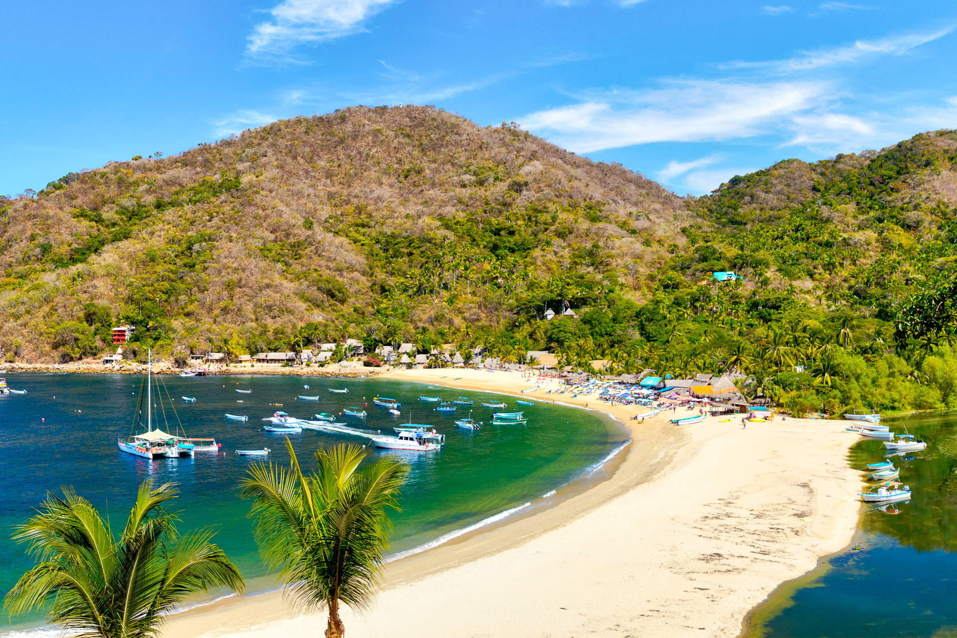 Plaża i zatoka w Yelapa w Meksyku. Na wodzie liczne łodzie, a w tle zielone wzgórze.