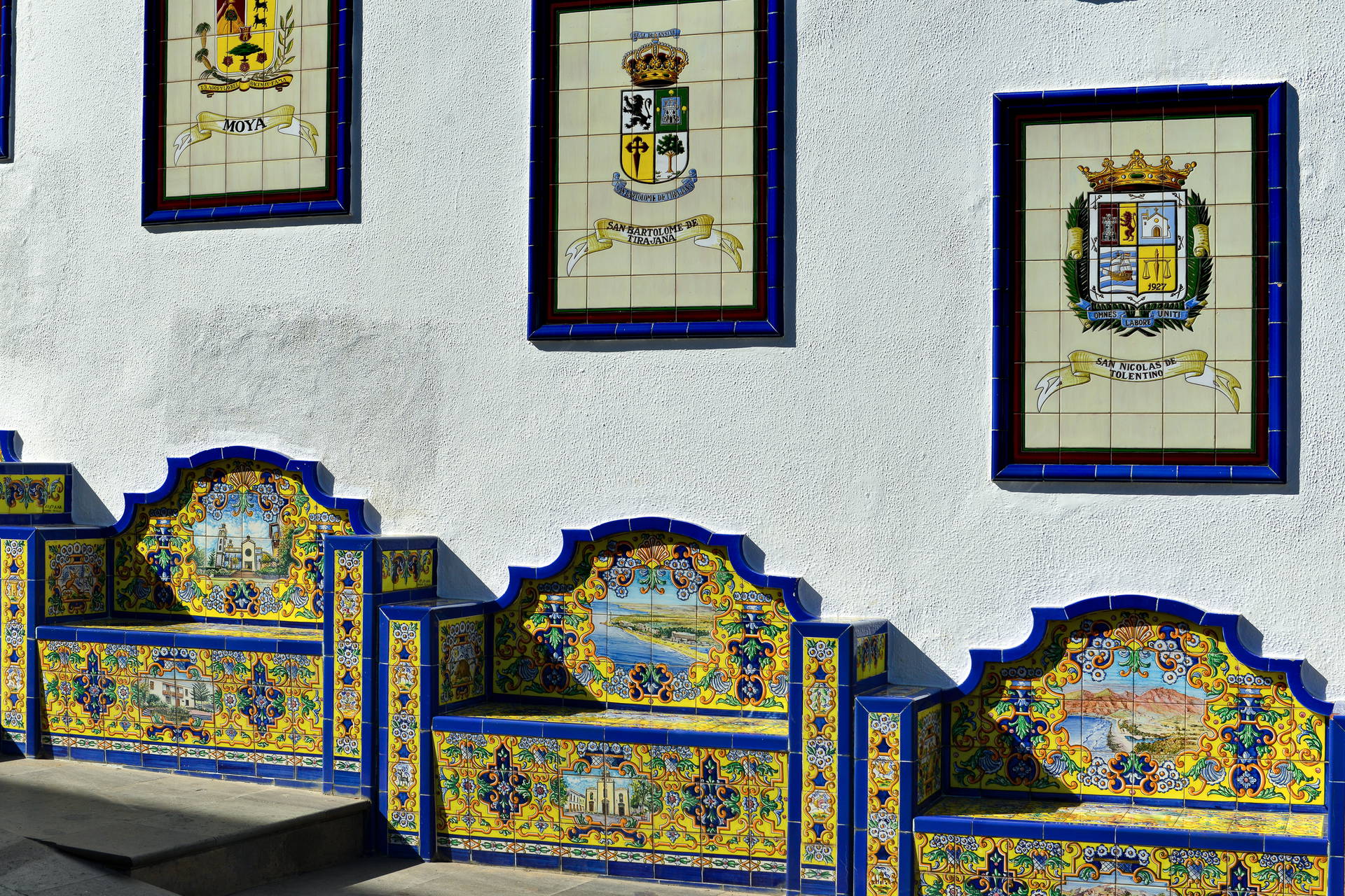 Kolorowe, ceramiczne ławki i herby ułożone z płytek na Paseo de Gran Canaria w Firgas.
