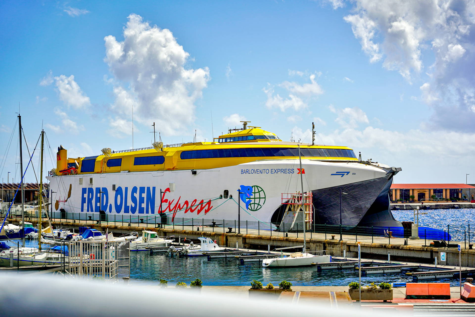 Biało-żółty katamaran pasażerski Barlovento Express, należący do Fred. Olsen Express, cumuje w porcie wśród mniejszych łodzi.