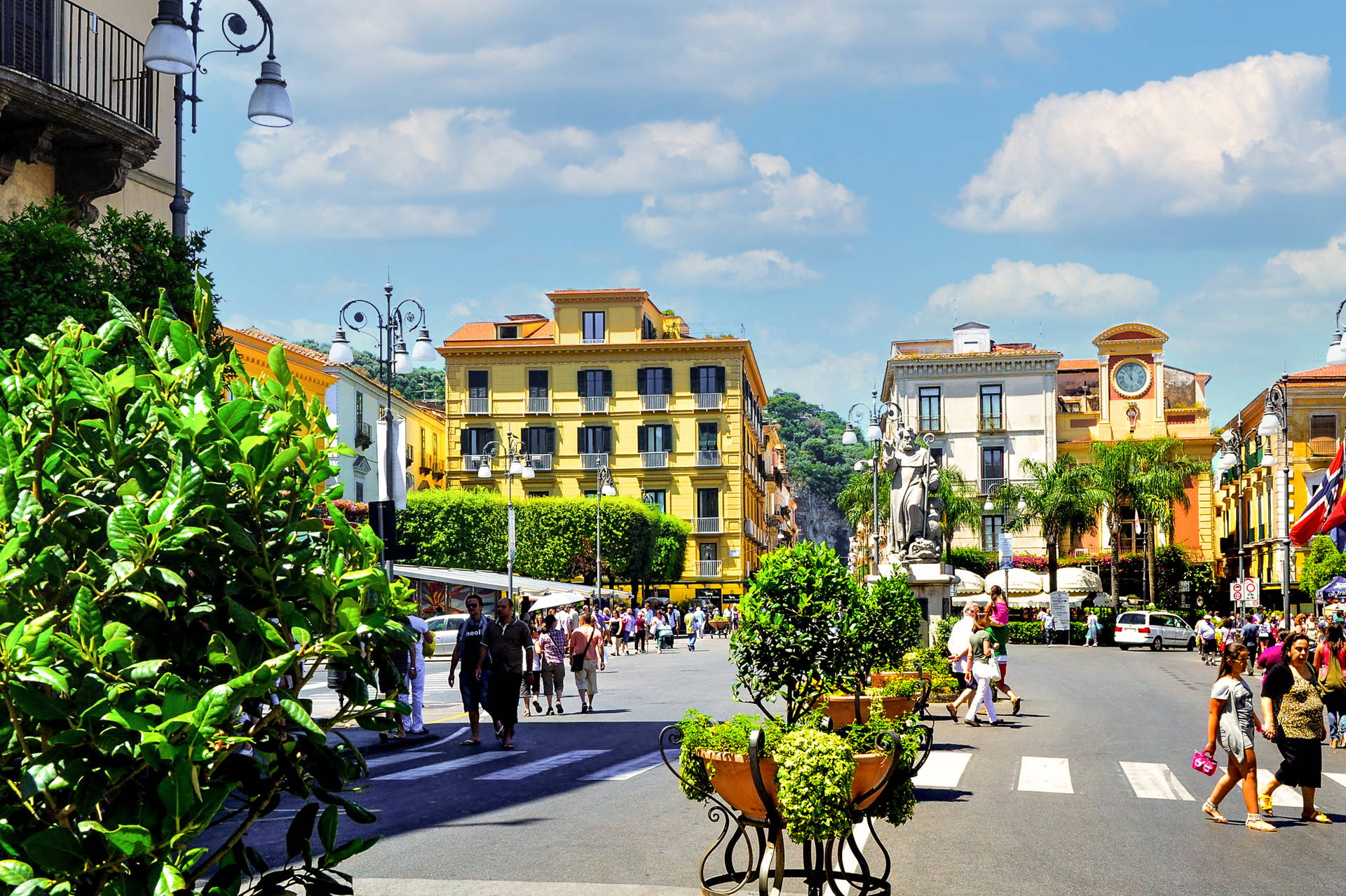 Plac Tasso w Sorrento tętni życiem w słoneczny dzień. Turyści przechodzą przez ulicę wśród kolorowych kamienic.