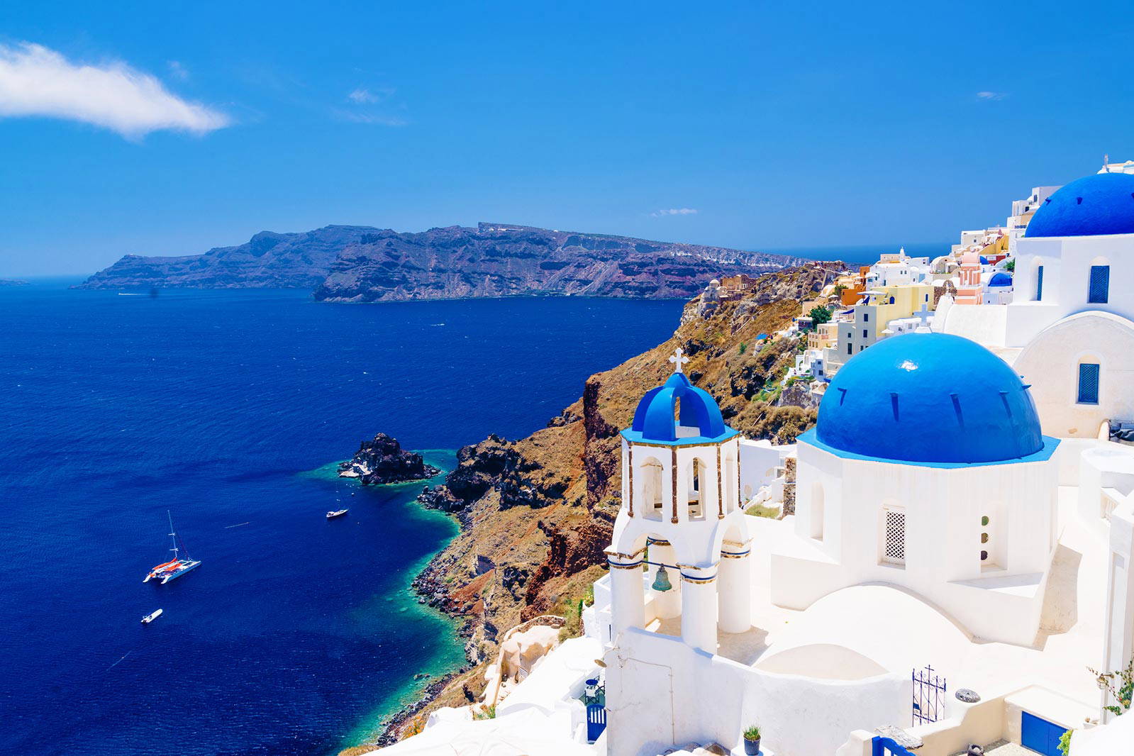 Białe budynki z niebieskimi kopułami na Santorini. W tle morze.