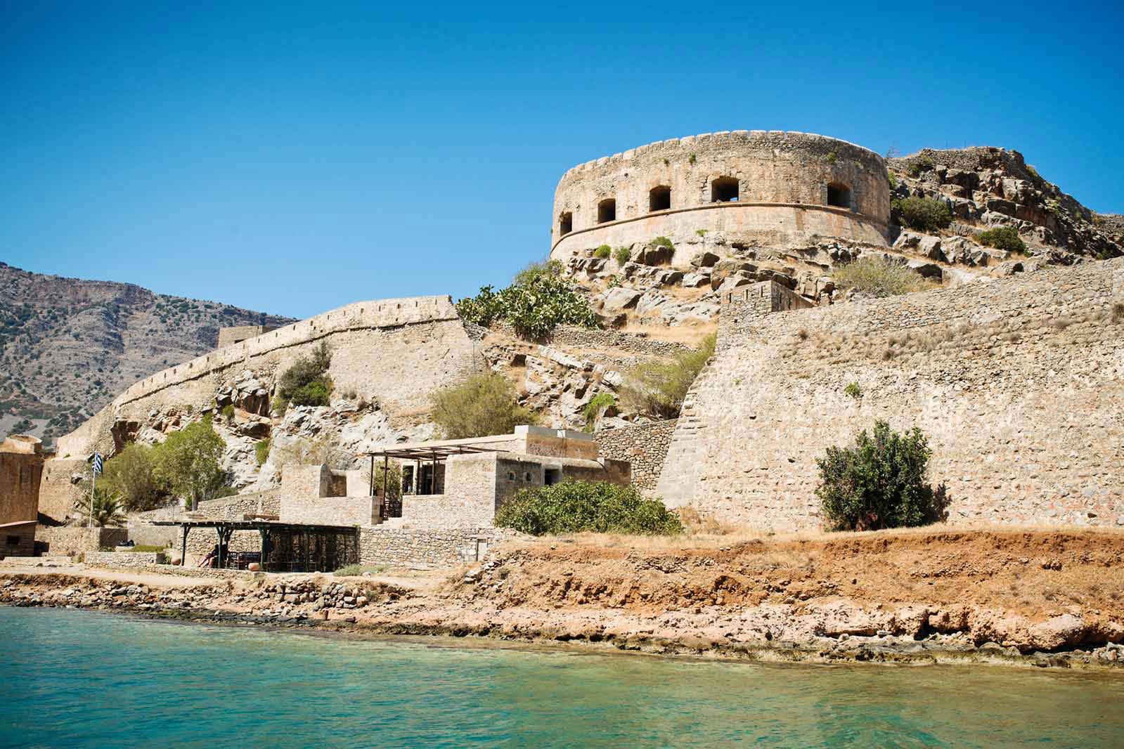 Spinalonga na Krecie. Kamienna forteca na wzgórzu i błękitna woda.