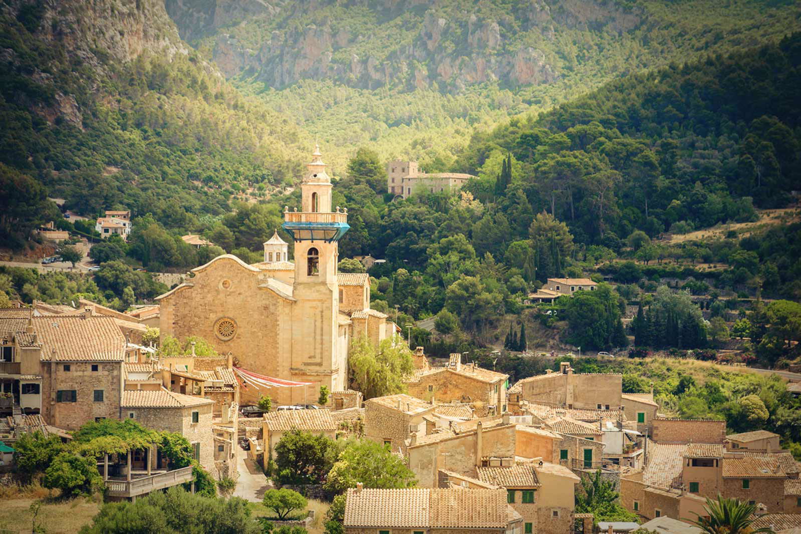 Valldemossa z kościołem w tle, otoczona zielonymi wzgórzami.