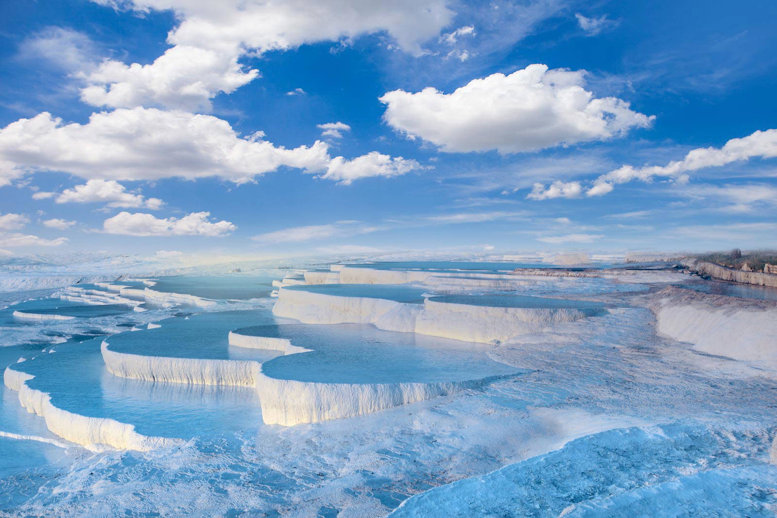 Pamukkale w Turcji: białe wapienne tarasy wypełnione wodą. W tle błękitne niebo z chmurami.