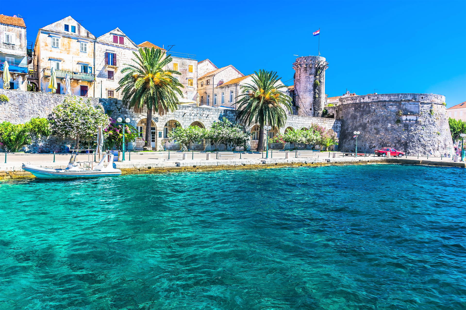 Trogir w Chorwacji: turkusowa woda, palmy na nabrzeżu i kamienna zabudowa.