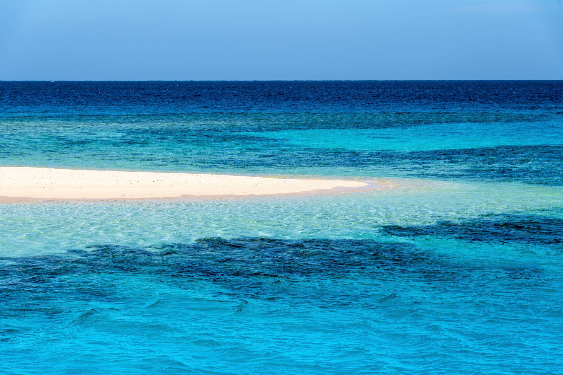 Błękitny ocean i mała, piaszczysta wyspa.