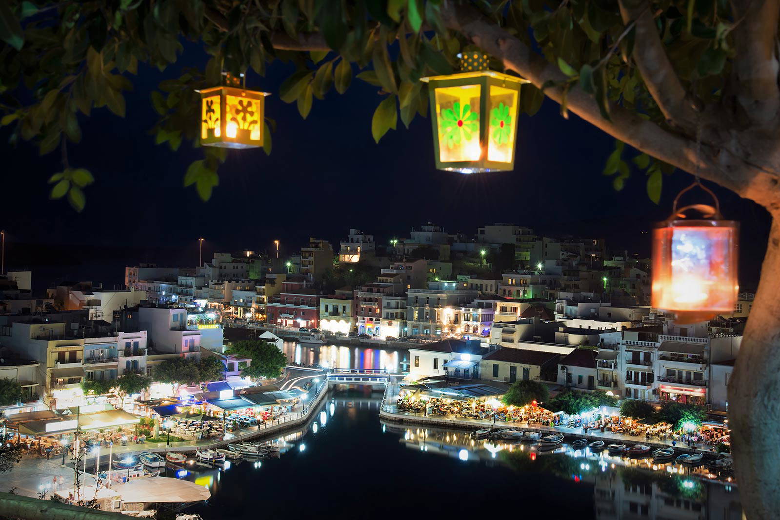 Nocny widok na jezioro Voulismeni w Agios Nikolaos z lampionami na drzewie.