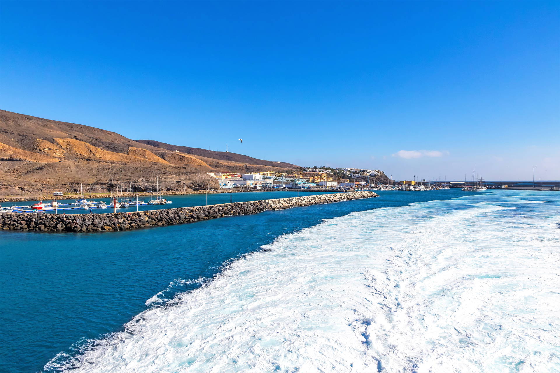 Marina w Morro Jable na Fuerteventurze. Widok na port, góry i ślad pozostawiony przez statek.