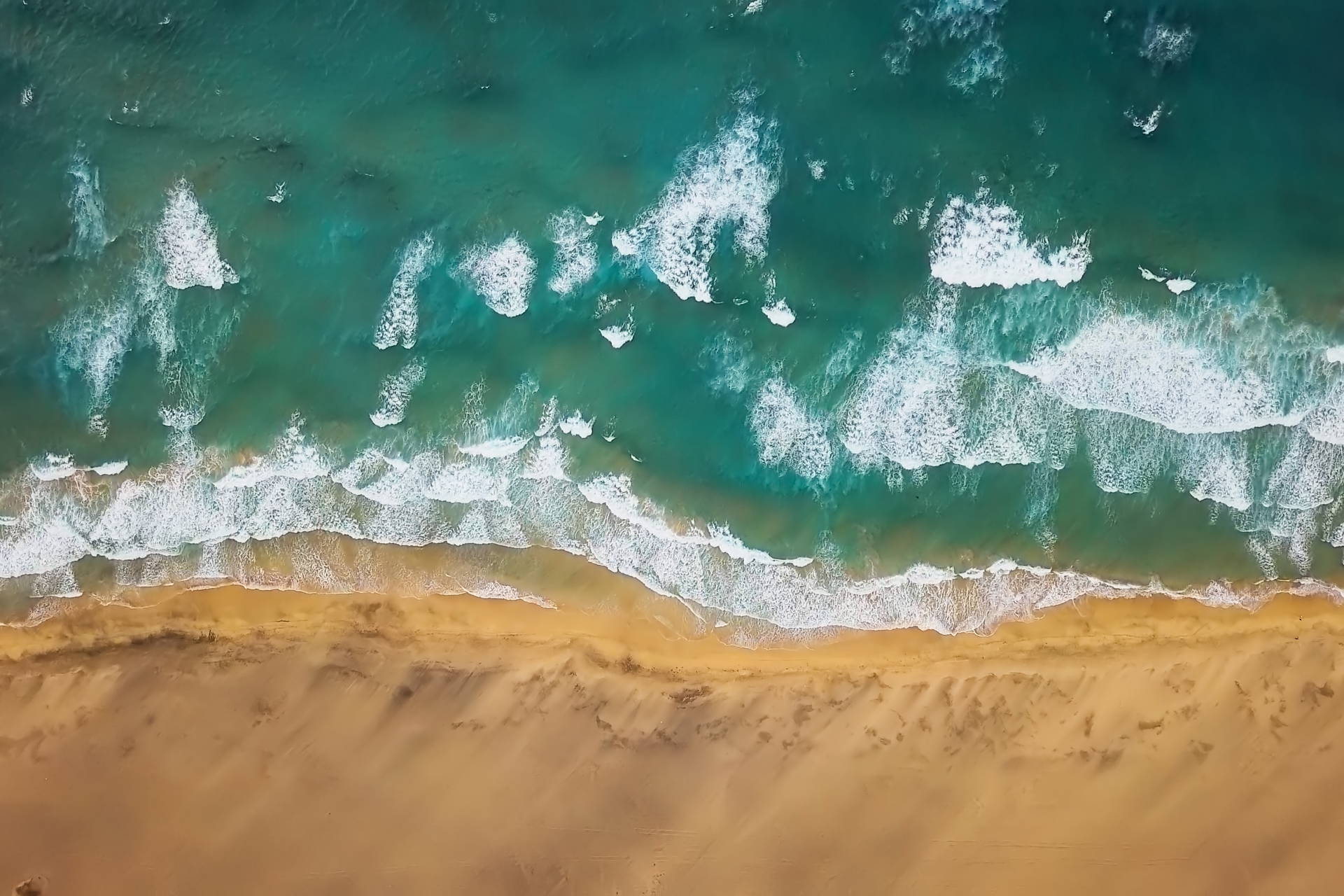 Piaszczysta plaża i turkusowy ocean z falami, widok z lotu ptaka.