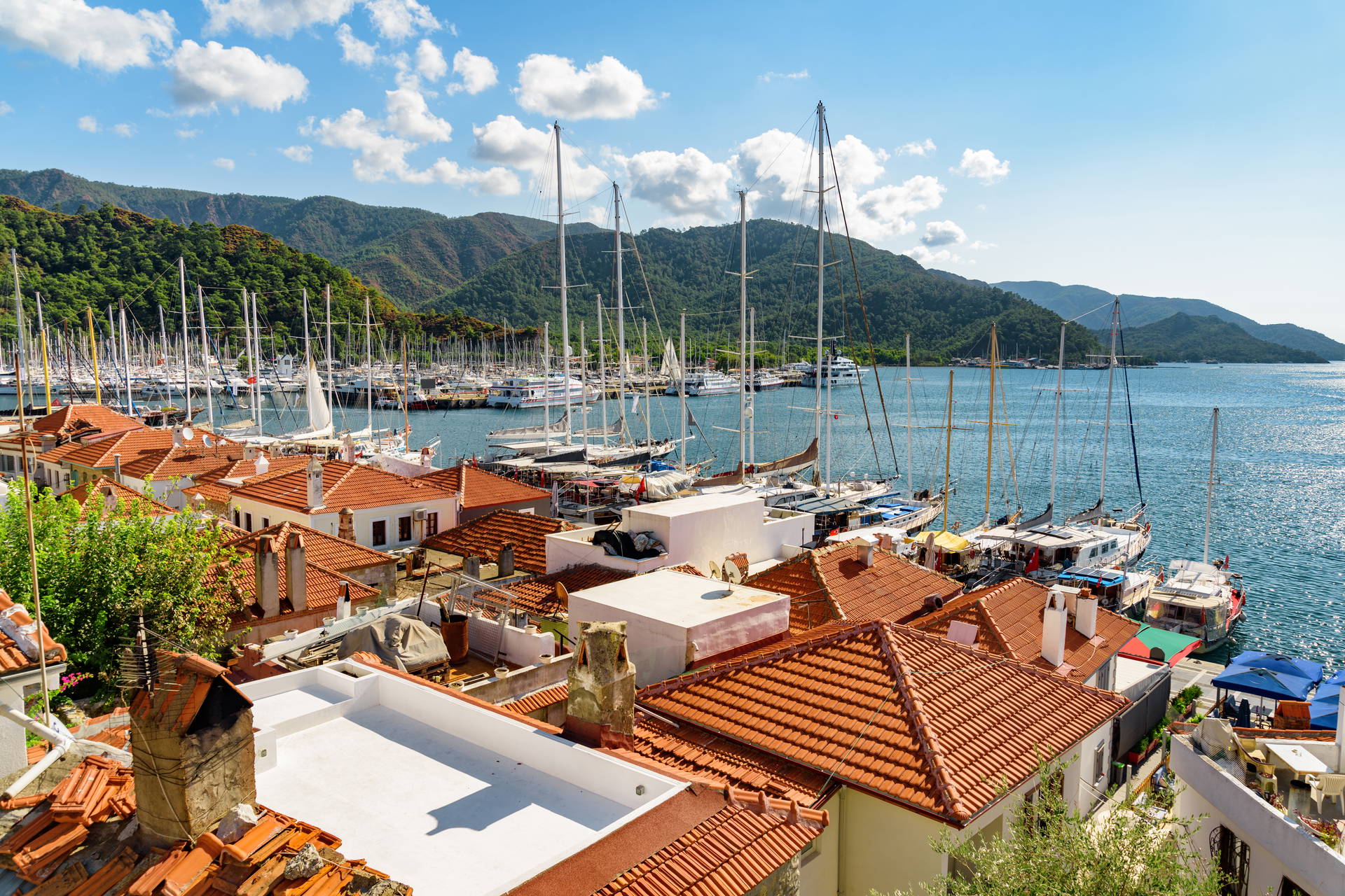 Port w Marmaris z czerwonymi dachami budynków i zacumowanymi jachtami.