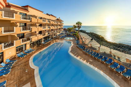 Hotel z basenem i ocean w tle widziany z góry.