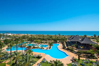 Resort z basenami i palmami, widok z góry. W tle ocean.