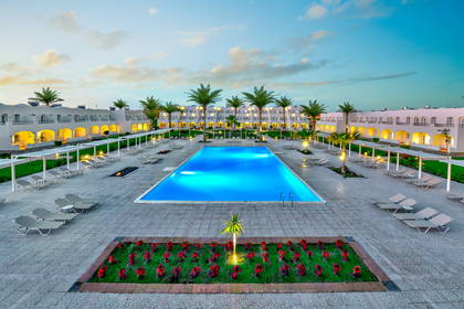 Hotel z basenem, leżakami i palmami.