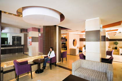 Hotelowe lobby. Kobieta siedzi na fotelu. Wnętrze zdobią dekoracje.