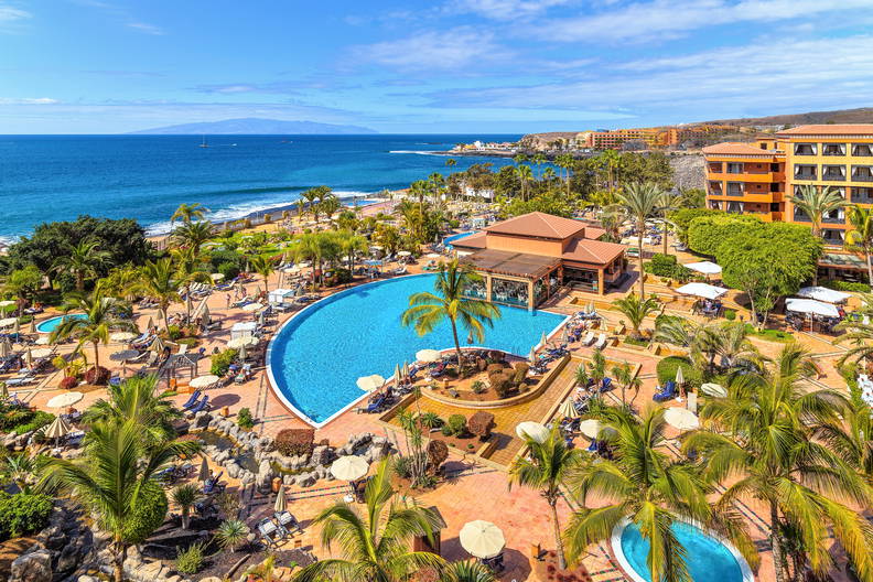 Luksusowy kurort z basenami i palmami, widok z góry na ocean.