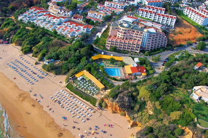 Zdjęcie lotnicze plaży z budynkami, basenem i parasolami przeciwsłonecznymi.