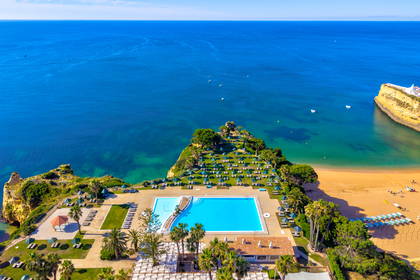 Widok z góry na hotelowy basen, taras z parasolami, plażę i klify nad błękitnym oceanem.