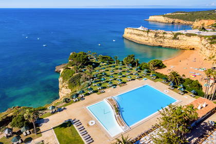 Widok z lotu ptaka na hotelowy basen przy piaszczystej plaży i klifach nad błękitnym oceanem w Algarve.