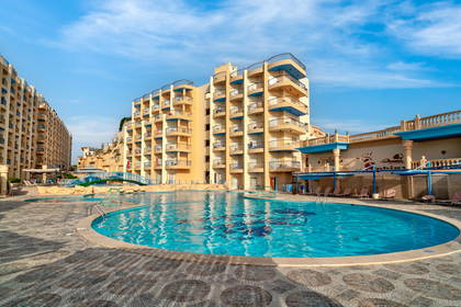 Kompleks hotelowy z basenem na tle błękitnego nieba.