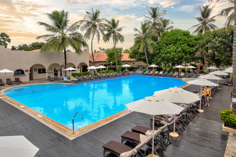 Basen z turkusową wodą otoczony palmami, leżakami i parasolami.