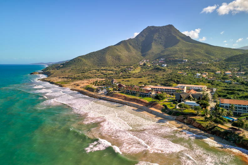 Widok z lotu ptaka na plażę, zabudowania i góry.